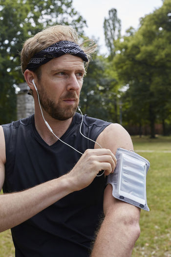 Man listening music while exercising against trees in park