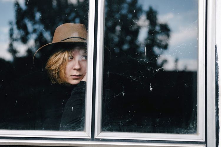 Modern girl with a hat looking trough the window, female outdoor portrai