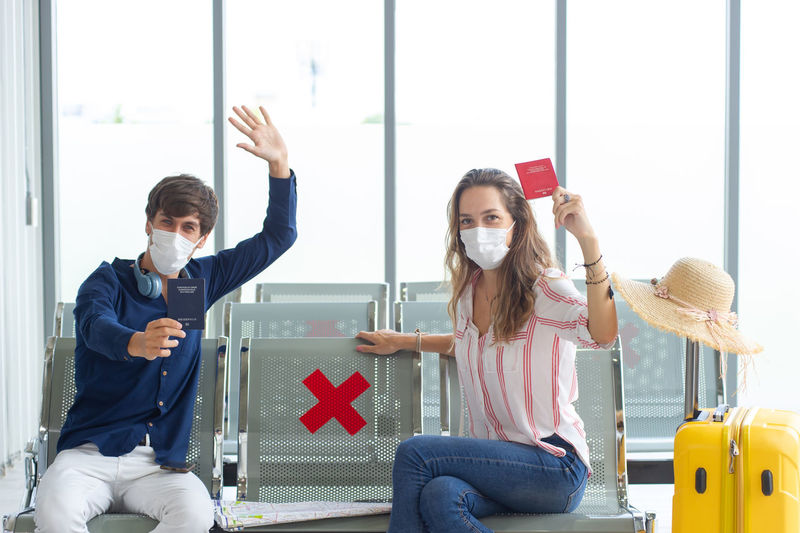 Portrait of smiling couple wearing flu mask showing passport at airport