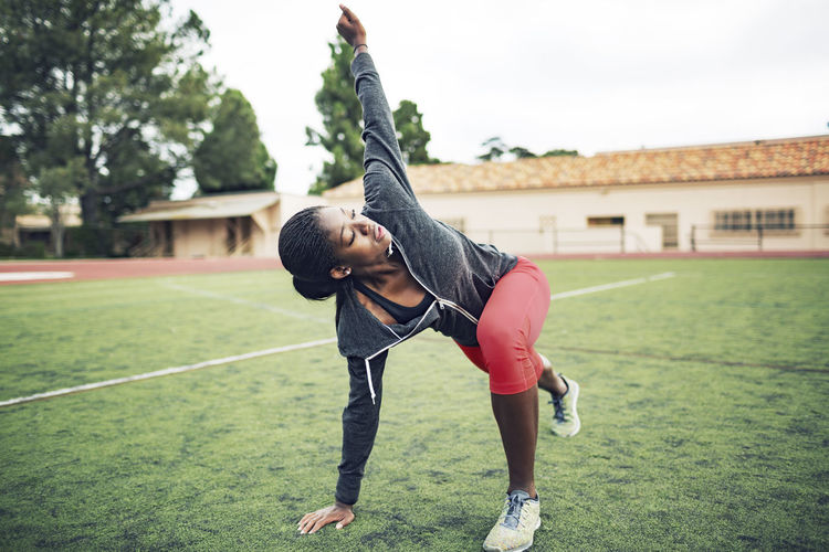 Determined female athlete doing stretching exercise on field