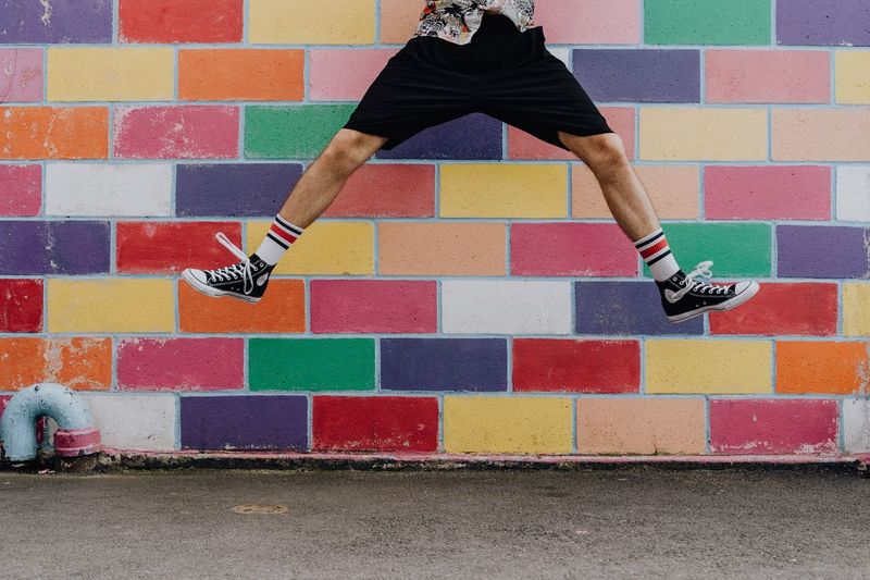 Low section of man jumping against colorful wall