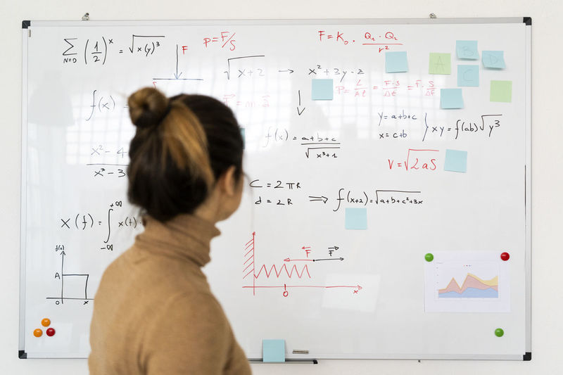 Woman analyzing mathematical formula written on whiteboard in living room