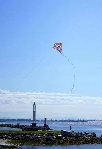 Kite flying over sea against clear blue sky