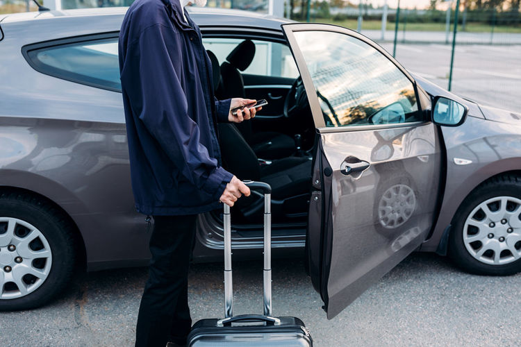 Man standing with luggage by car parked in city
