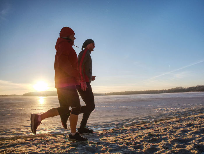 Fitnes couple man and woman. winter landscape with sun at horizon. frozen river makes reflection.