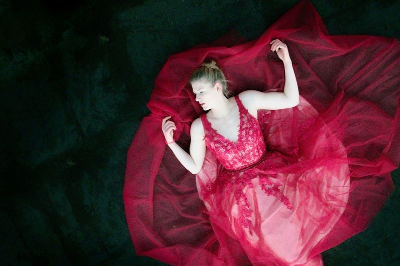 High angle view of young woman in red dress lying on floor