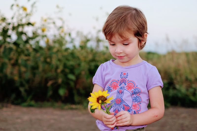 Close-up of girl holding flower while standing on field