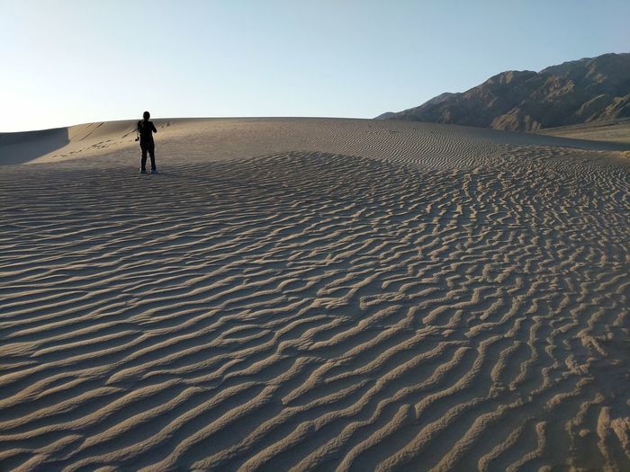 Scenic view of a woman standing on a sand dune in desert against clear sky