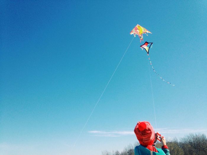 Rear view of person flying kite against clear blue sky
