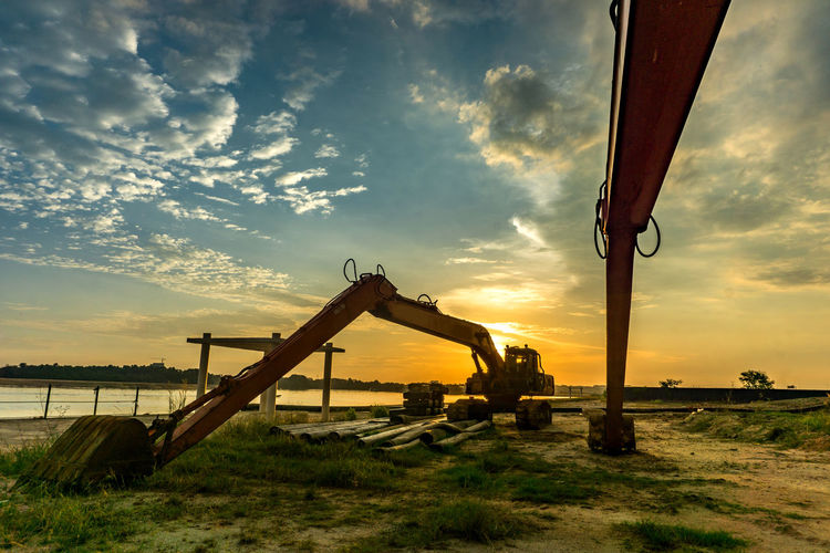 Bulldozers on field against sky during sunset