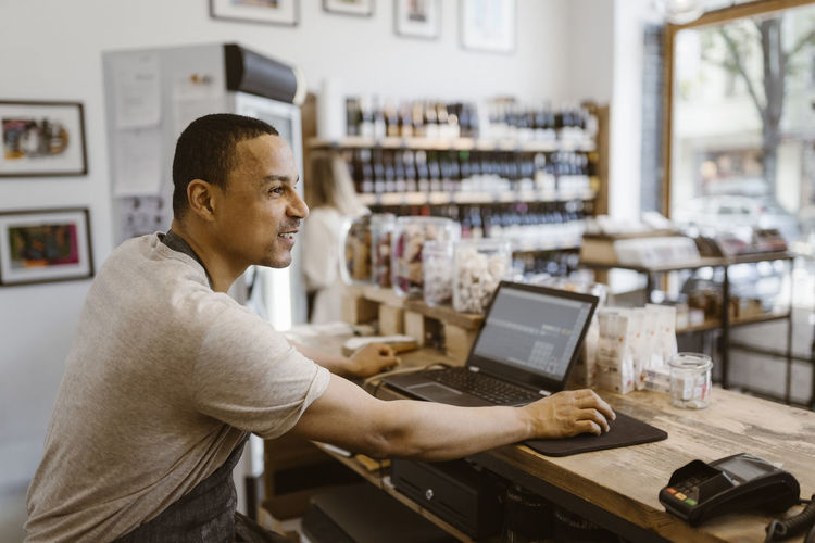 Side view of male owner sitting at checkout counter in deli