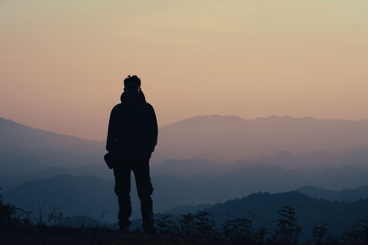 Rear view of silhouette man standing against mountain during sunset