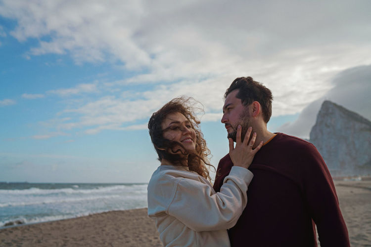 Couple standing at beach against cloudy sky