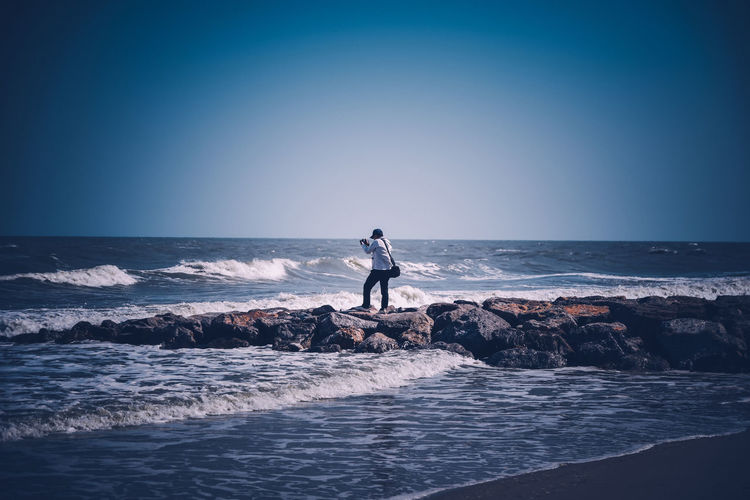 Man standing on rock in sea against sky