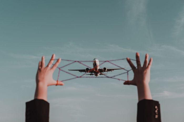 Cropped hands holding string against airplane flying in sky