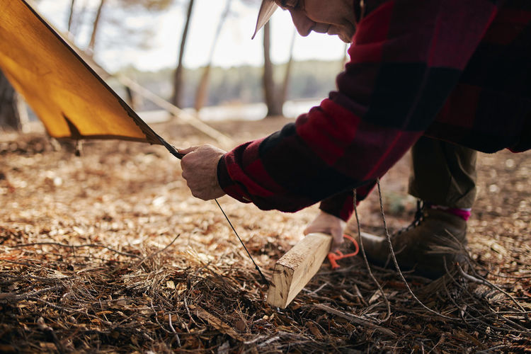 Midsection of bushcrafter preparing tent in forest