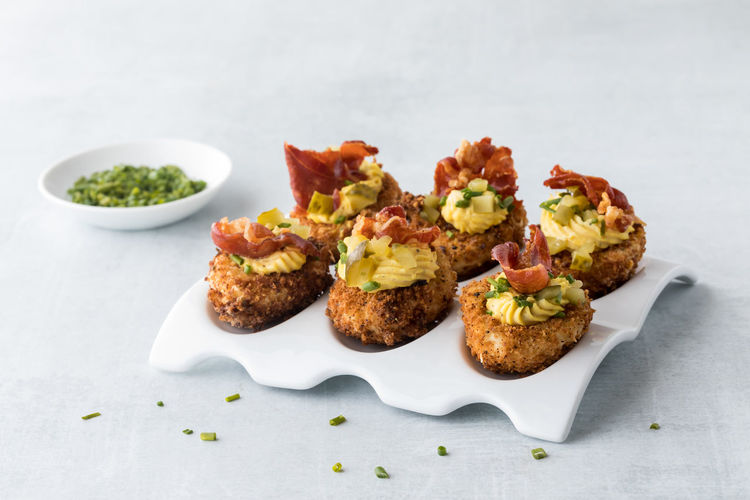 A white platter of deep fried deviled eggs garnished with chives and prosciutto