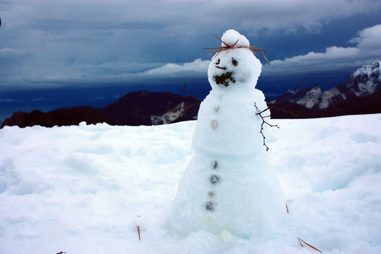 White snowman with twigs and stones and the panorama of apuan alps between mountains and blue sea