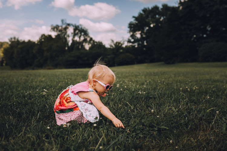 Cute toddler girl crouching on grassy field