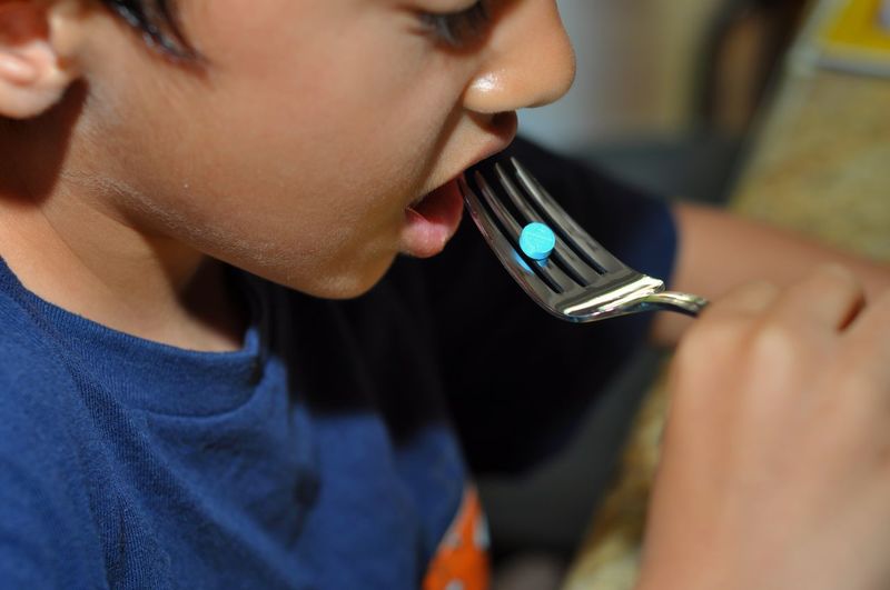 Close-up of boy eating blue pill from fork at home