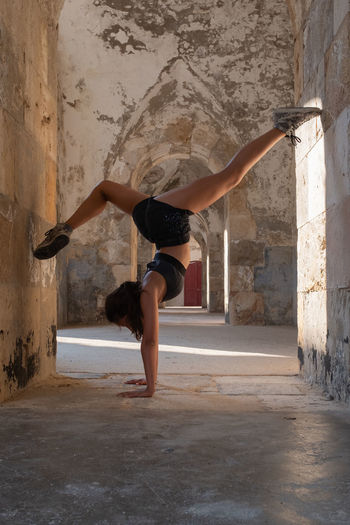 Young woman performs handstands with split legs.