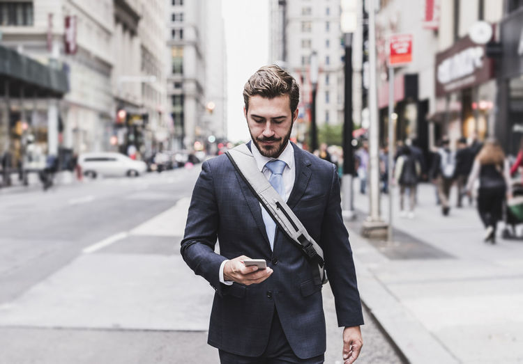 Usa, new york city, businessman walking in manhattan looking at cell phone