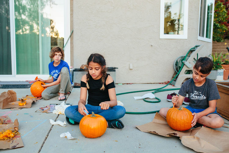 Two sisters and brother carve pumpkins outside