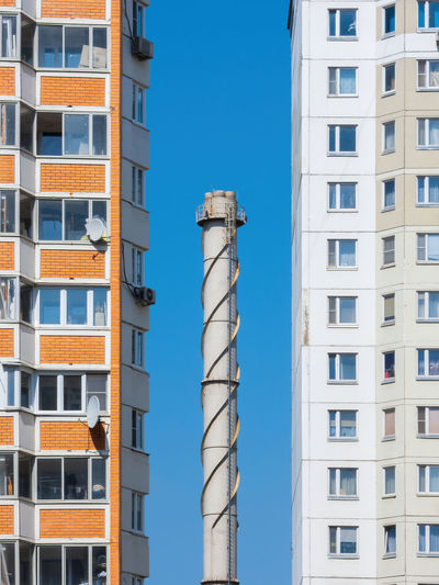 Chimney tube against a blue sky surrounded by apartment buildings