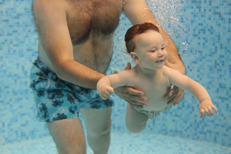 Midsection of father with son in swimming pool