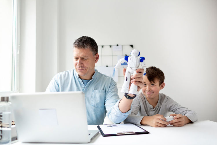 Man teaching son with robot while using laptop on table