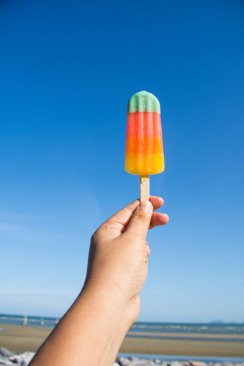 Close-up of hand holding popsicle against blue sky