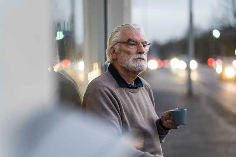 Senior man with eyeglasses holding coffee cup while sitting outside cafe