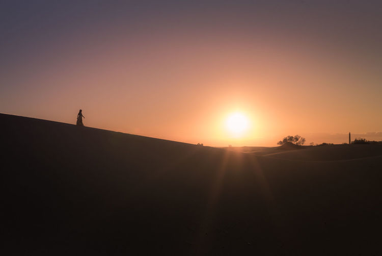 Silhouette woman standing on sand dune against clear sky during sunset