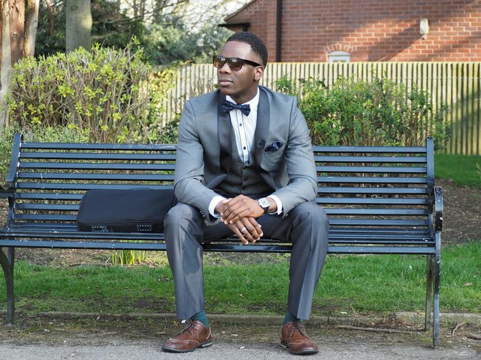 Young man in full suit sitting on park bench