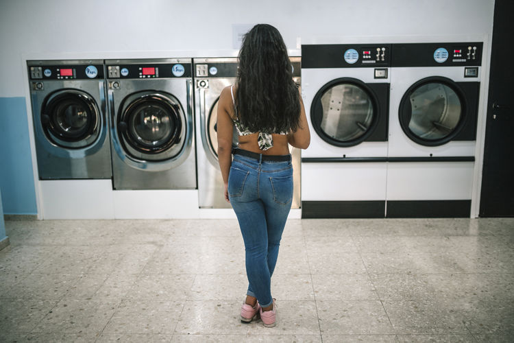 Rear view of teenage girl standing by washing machines at laundromat