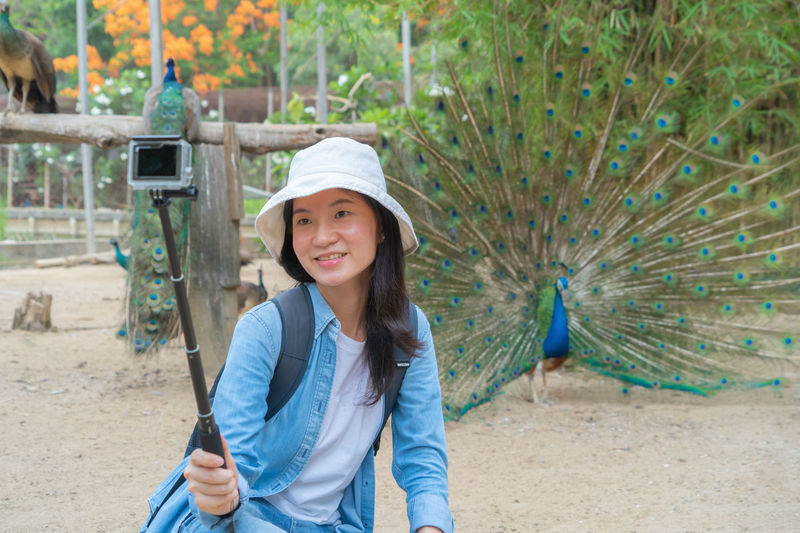 Smiling woman recording video against peacock