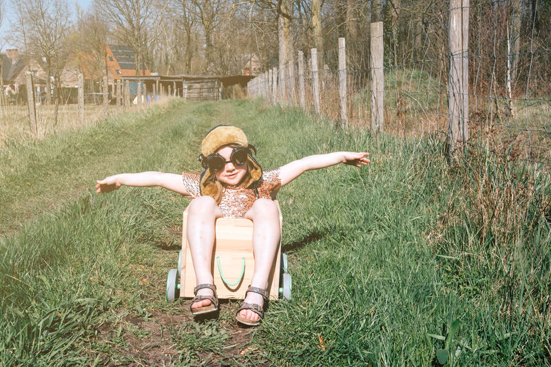 Childhood freedom - happy girl with aviator cap dreaming of flying in a wooden box with wheels