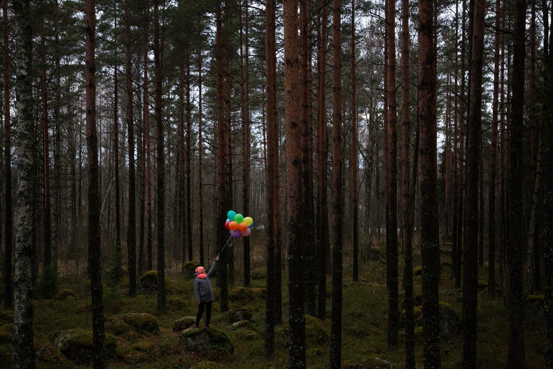 Woman holding balloons standing amidst trees in forest