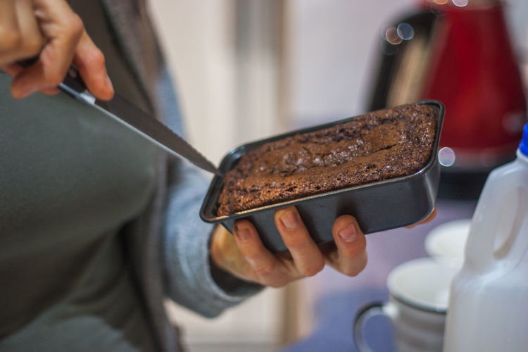 Midsection of woman cutting chocolate cake at home