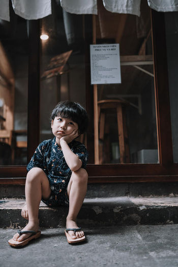 Sad boy looking away while sitting on footpath