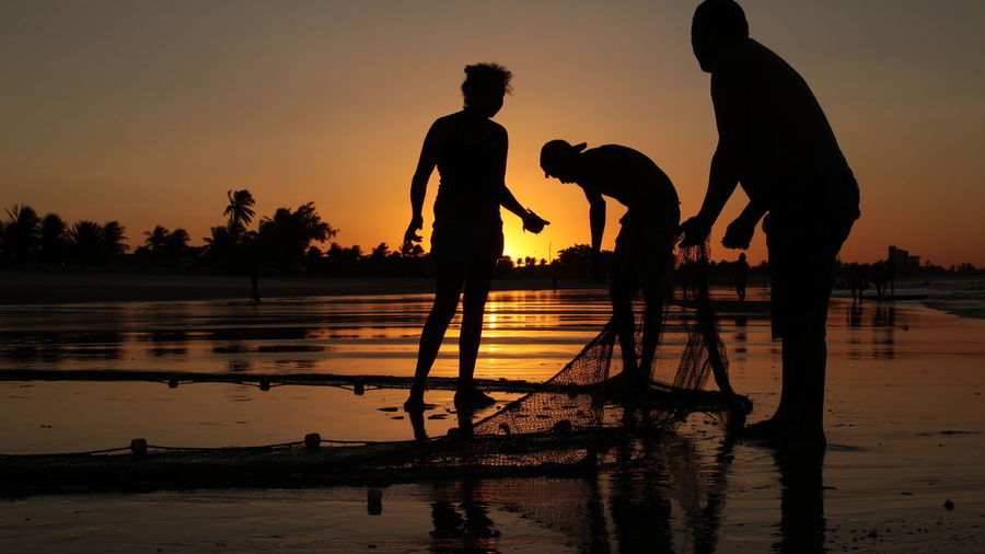Silhouette fishermen at shore during sunset