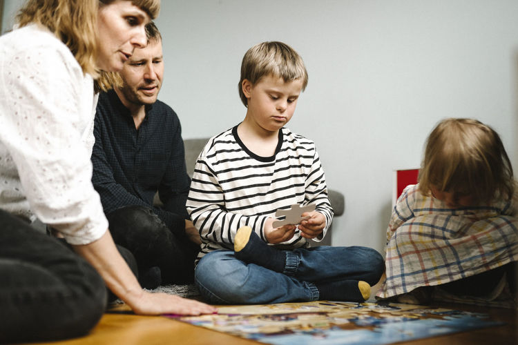 Boy having disability joining jigsaw pieces sitting with family at home