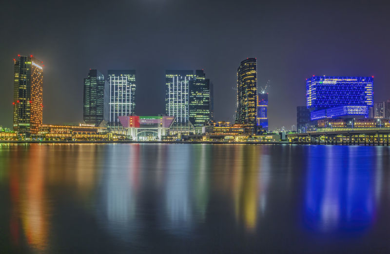 Illuminated buildings by river against sky at night