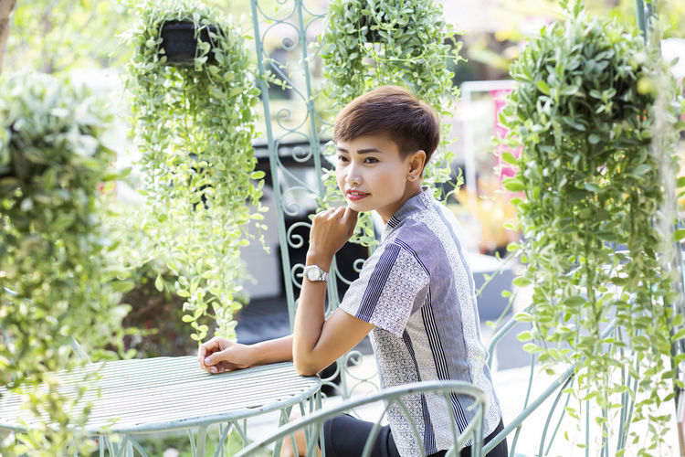 Boy looking away while sitting on plants outdoors