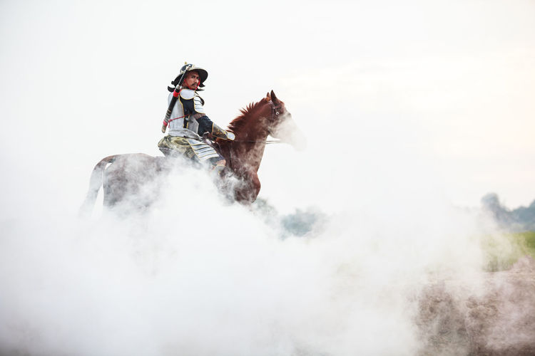 Low angle view of warrior riding horse in foggy weather