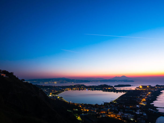 Aerial view of illuminated city buildings against sky at sunset