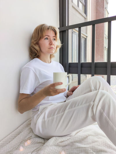 Young woman drinking coffee cup on bed at home