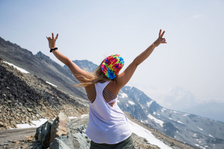 Girl poses with peace sign on top of mountain in summer
