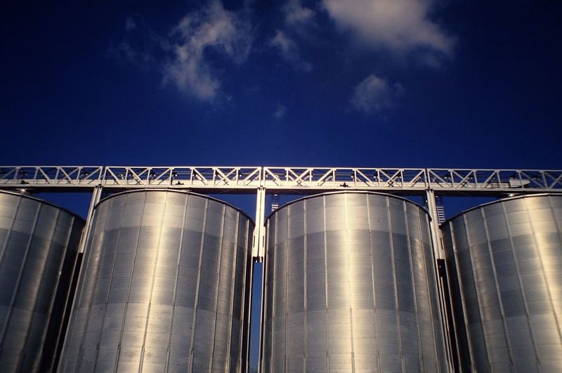 Low angle view of shiny silos against blue sky