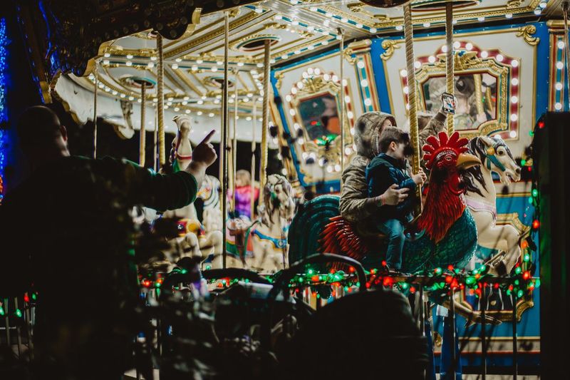 Mother taking selfie with son while sitting in carousel at amusement park during night